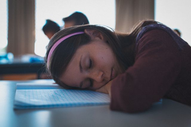 Young student resting her head on a notebook at her desk in a classroom. Ideal for illustrating themes of childhood education, student fatigue, concentration challenges, and the need for breaks in learning environments.