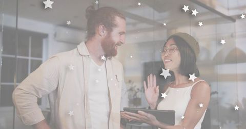 Creative coworkers collaborating on tablet in modern glass office with playful star overlay