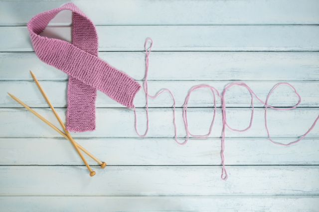 Overhead view of pink Breast Cancer Awareness ribbon by hope text and crochet needles on white wooden table