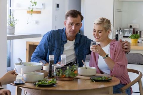 Couple enjoying casual home lunch at sunlit kitchen table, sharing salad and smiling