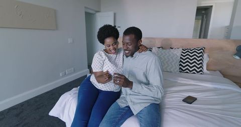 African american couple opening small gift box on bed celebrating intimate moment
