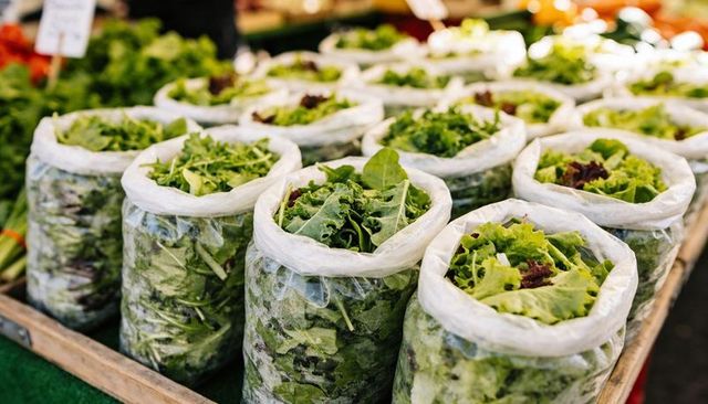 Displaying clear plastic bags holding mixed salad greens on wooden crate at farmers market