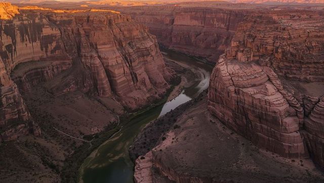 Golden hour over meandering green river cutting through red sandstone canyon cliffs