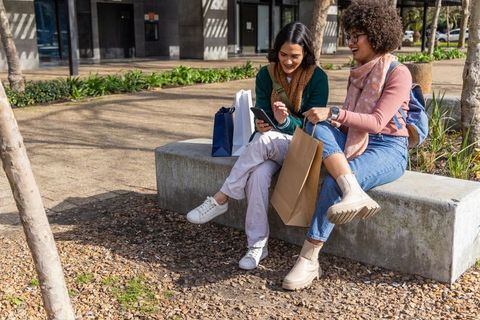Sharing laughs and shopping finds on urban bench during sunny city outing