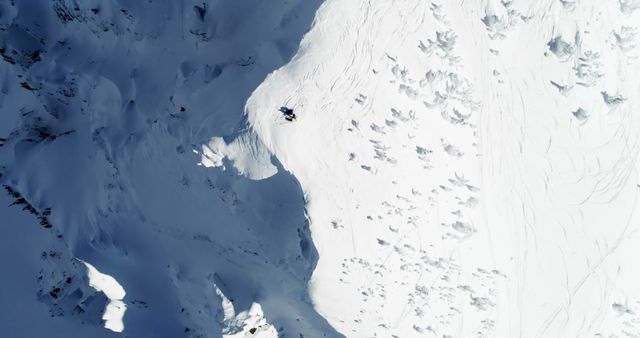 A top-down view of skiers gliding on a steep, snowy mountain slope. Perfect for promoting winter sports, adventure trips, or winter apparel brands. Can be used in magazines, travel blogs, or advertisements related to skiing and snowboarding.