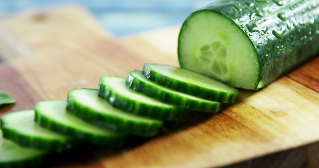 Sliced cucumber rests on a wooden cutting board, showcasing a fresh and healthy ingredient choice. Its vibrant green color emphasizes the freshness and nutritional value of the vegetable.