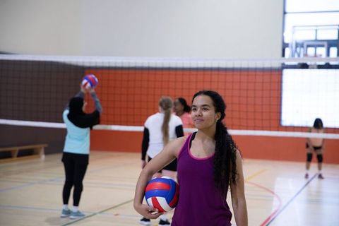Teen girl holding volleyball and leading indoor team practice on school sports court