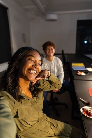 Smiling diverse coworkers taking selfie in modern office during after-hours teamwork
