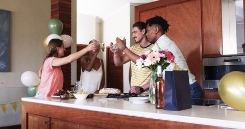 Friends Celebrating in Modern Kitchen with Drinks and Snacks