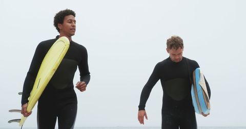 Two male surfers running with boards on sandy beach