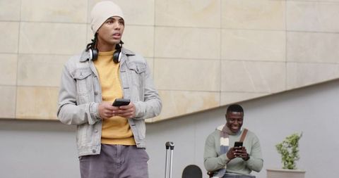 Urban young travelers checking phones at transit plaza with luggage and skateboard