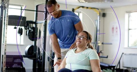 Wheelchair user smiling while trainer providing shoulder support during gym rehabilitation