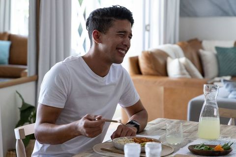 African american man laughing while enjoying casual homemade lunch at bright dining table