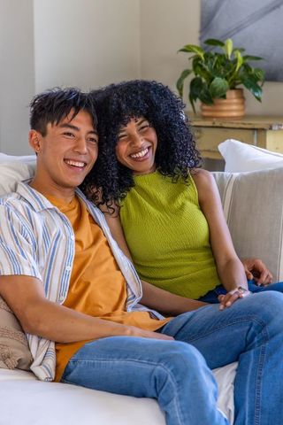 Smiling diverse couple relaxing on light sofa, leaning together and enjoying cozy moment