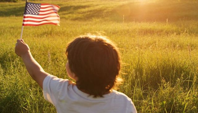 Child waving american flag in sunlit meadow at golden hour