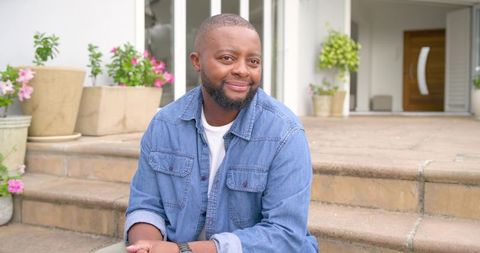 African american man mid-30s relaxing on front steps wearing denim shirt and watch
