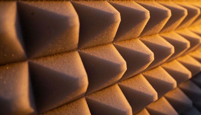 Pyramid foam panels catching warm side light and dust, geometric acoustic texture