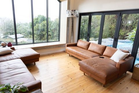 Sunlit contemporary living room featuring tan leather sectional, wooden floor, pool view