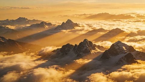 Golden sunrise casting long shadows over snow-capped alpine peaks above cloud inversion