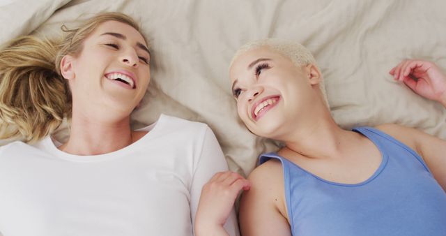 Happy diverse female couple embracing and lying together in bed. spending quality time at home.