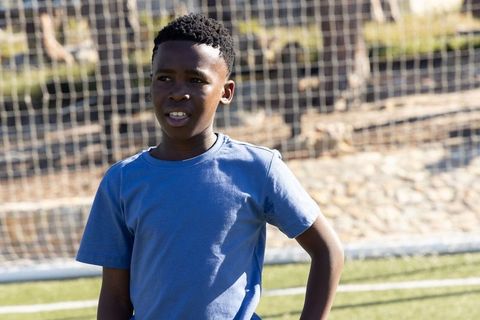 African american boy standing on soccer field near goal net wearing blue t-shirt