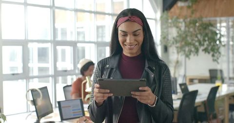 Indian woman smiling using tablet in modern coworking office with diverse team
