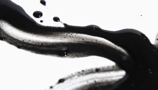 Flowing black ink smear on white paper, glossy droplets and speckled pigment texture