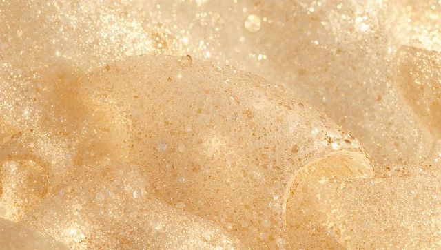 Glittering golden-beige foam macro revealing microbubbles and sparkling froth texture