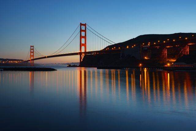 Golden Gate Bridge spanning San Francisco Bay, illuminated against twilight sky. Ideal for travel blogs, tourism websites, or promotional material for San Francisco. Highlights iconic architecture and serene evening atmosphere.