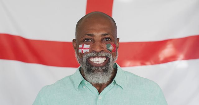 Man proudly showing England flag face paint while smiling. Can be used for representing national pride, promoting sports events, celebrating multicultural support, or patriotic advertisements.