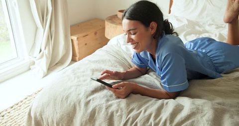 Woman Enjoying Smartphone Leisure in Sunlit Bedroom