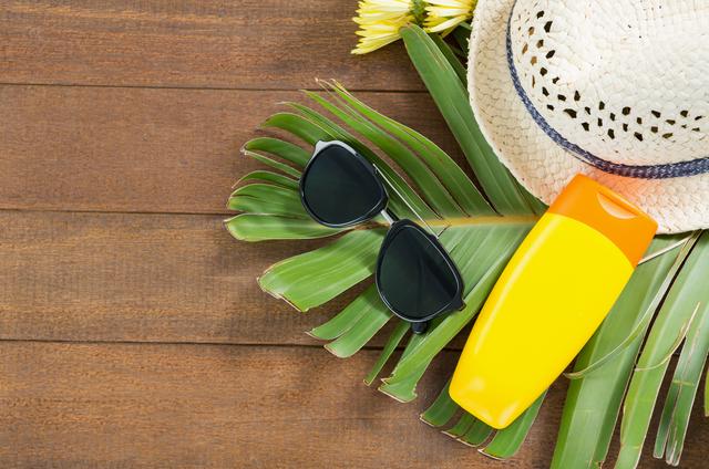 Sunglasses, sunscreen, and a straw hat placed on palm leaves over a wooden board. Ideal for promoting summer vacations, beach holidays, travel essentials, and sun protection products. Perfect for travel blogs, holiday brochures, and advertisements for summer accessories.