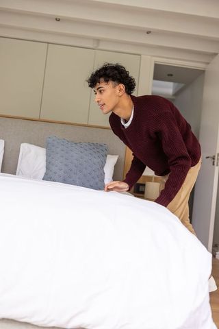 Man making bed in minimalist bedroom interior for comfort and tranquility