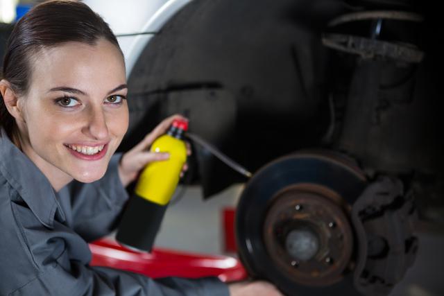 Portrait of beautiful female mechanic oiling a car brake at repair garage