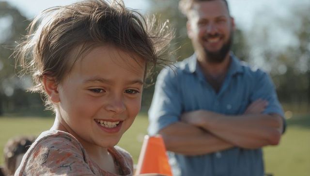 Smiling boy holding orange cone with father watching, outdoor play in park