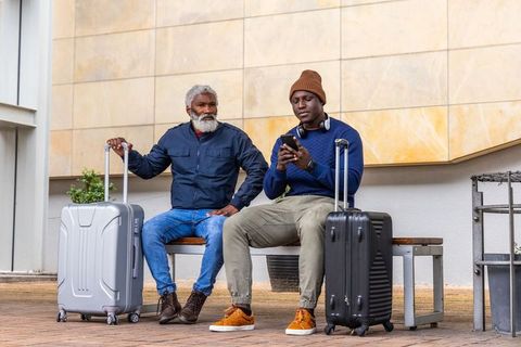 African american men waiting at transit hub with suitcases and smartphone, urban travel