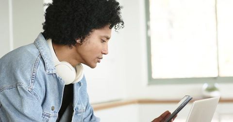 African American man using tablet and laptop with headphones in bright minimalist home office