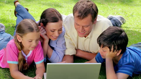 Happy Family Enjoying Outdoor Time with Laptop in Park