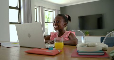 African girl learning online at home smiling while using laptop for schoolwork