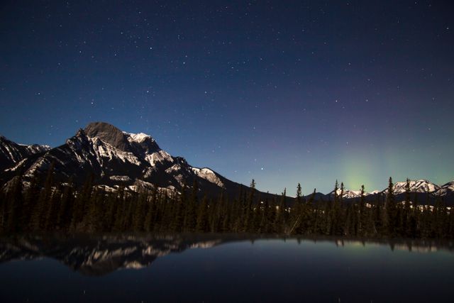 Night sky over a mountain lake with visible aurora borealis. Stars filling the sky and the mountains reflecting in the calm waters. Ideal for nature, travel, astronomy, and landscape projects.