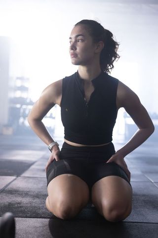Kneeling athlete pausing between sets in backlit gym wearing black crop top and shorts