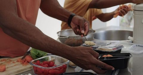 African american man and teenage boy packing healthy meal prep containers in kitchen