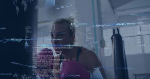 Mid-adult woman training boxing with pink gloves in industrial gym, digital hud overlay