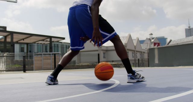 Man dribbling basketball on urban outdoor court. Ideal for promoting sports, athleticism, basketball training, youth sports development, and active lifestyle.