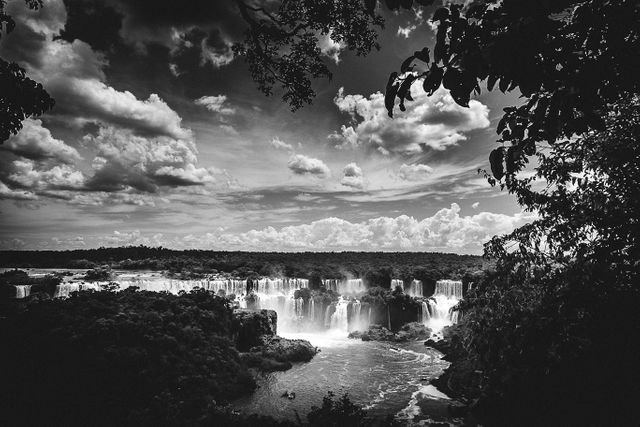 This powerful waterfall scene captured in black and white highlights the dramatic contrast between the cascading water, the swirling clouds, and the surrounding foliage. This versatile image is excellent for nature magazines, travel blogs, environmental campaign materials, and publications seeking to evoke the majesty and power of natural landscapes.