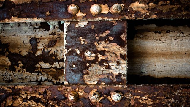 Textural photo depicting a close-up of an oxidized metal surface with rust and peeling paint. Rust spots and corrosion detail illustrate weathering. Great for backgrounds, overlays, industrial themes, and materials science studies.