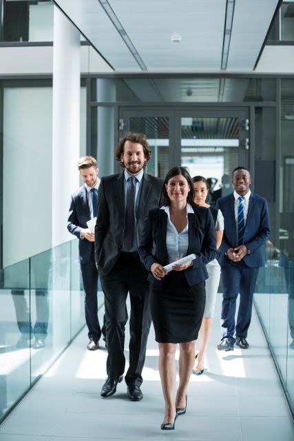 Businesswoman leading a group of colleagues in a modern office environment. Ideal for use in corporate websites, business presentations, and promotional materials highlighting teamwork, leadership, and professional settings.