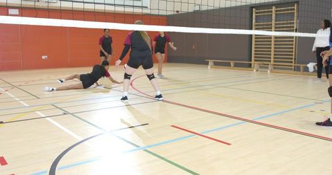 Female volleyball players diving for ball in indoor gymnasium during competitive match
