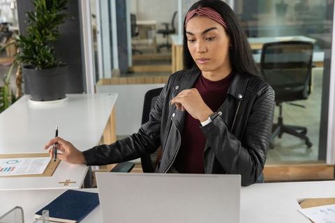 Young professional woman working on laptop in modern open-plan office, focused and organized