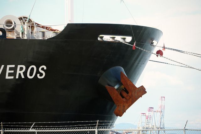 Docked cargo ship with a rusty anchor prominently displayed at a port. The ship's black hull and maritime equipment are visible. Ideal for topics related to shipping, sea transport, logistics, and maritime industry themes.